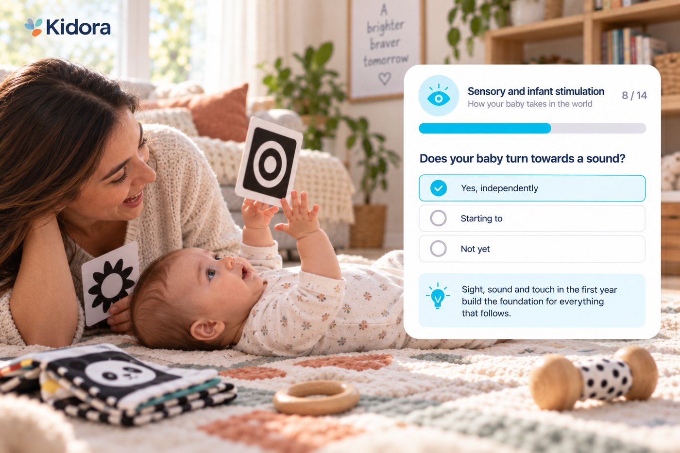 A mother lies on a rug beside her baby, holding a black and white contrast card just within reach as the baby looks up and reaches for it. A Kidora card shows a sensory and infant stimulation score of 8 out of 14.